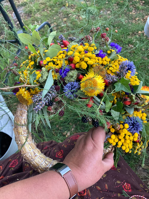 Halb gebundener Herbstkranz aus gelben und blauen Blüten, Gräsern und Beeren auf einem Strohrohling